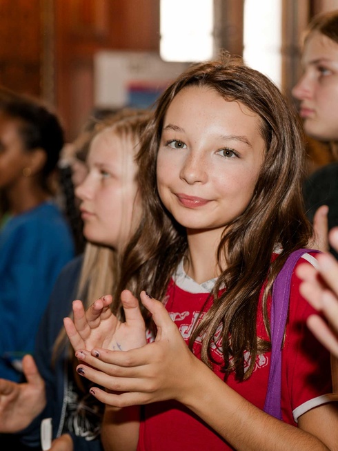 Ein Mädchen in rotem Shirt applaudiert, umgeben von anderen Jugendlichen.