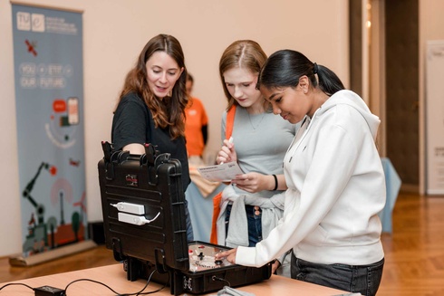 Drei Frauen erkunden gemeinsam ein technisches Gerät auf einem Tisch.