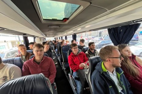 Innenansicht eines Busses mit mehreren Fahrgästen, die sitzen und miteinander sprechen.