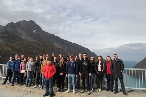 Gruppe von Menschen, die vor einer Berglandschaft an einem Aussichtspunkt stehen.