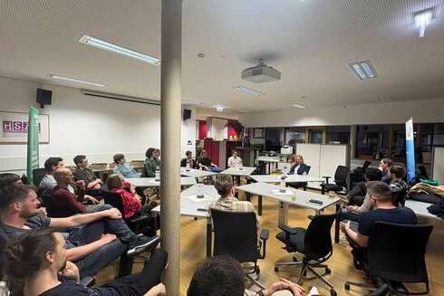 Gruppe von Menschen in einem Raum, die einer Diskussion oder Präsentation folgen.