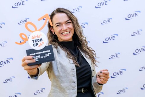 Eine lächelnde Frau präsentiert stolz einen Preis für den Girls! Tech Up Wettbewerb.