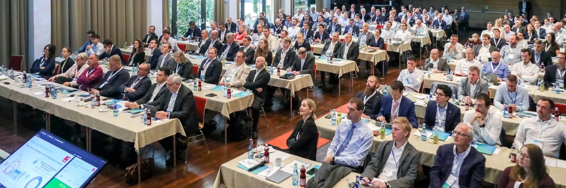Ein großes Publikum sitzt an Tischen in einem Konferenzsaal.