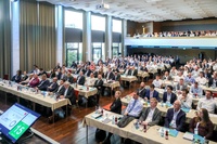 Ein großes Publikum sitzt an Tischen in einem Konferenzsaal.