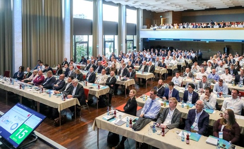 Ein großes Publikum sitzt an Tischen in einem Konferenzsaal.
