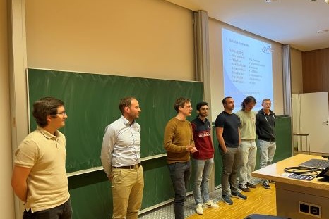Sechs Personen stehen vor einer Tafel in einem Seminarraum.