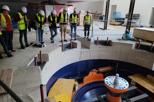 Eine Gruppe von Personen betrachtet eine große Maschine in einem Bauwerk.