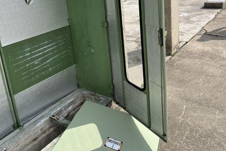Ein offenes, grünes Gebäude mit einem abgenommenen Schild auf dem Boden.