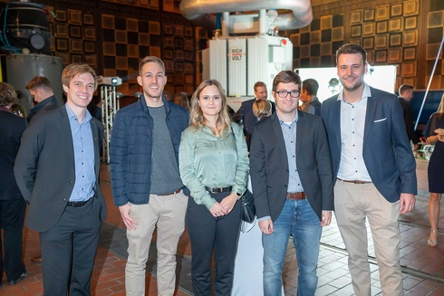 Fünf Personen posieren lachend bei einer Veranstaltung in einem Innenraum.