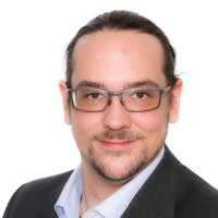 Porträt eines Mannes mit Brille in einem Anzug, freundlich lächelnd.