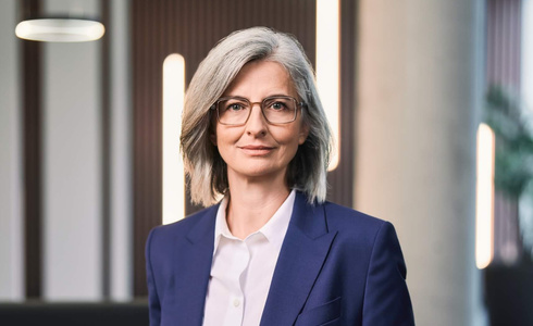 Eine Frau mit grauen Haaren und Brille trägt einen blauen Blazer.