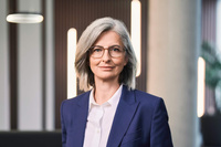 Eine Frau mit grauen Haaren und Brille trägt einen blauen Blazer.