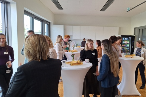 Gruppendiskussion in einem modernen Raum mit Stehtischen und Snacks.