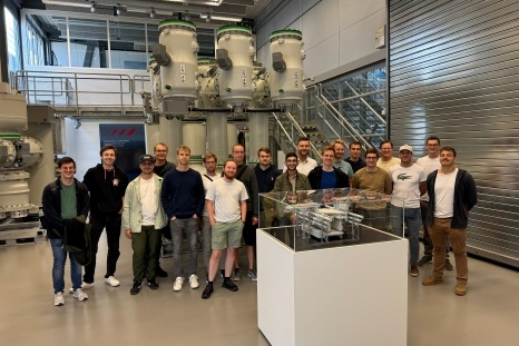 Gruppe von Menschen steht in einer modernen Industrieumgebung vor einem Ausstellungsstück.