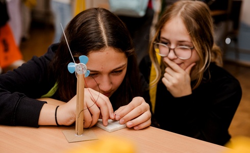 Zwei Mädchen bauen gemeinsam ein kleines Windrad aus Materialien.