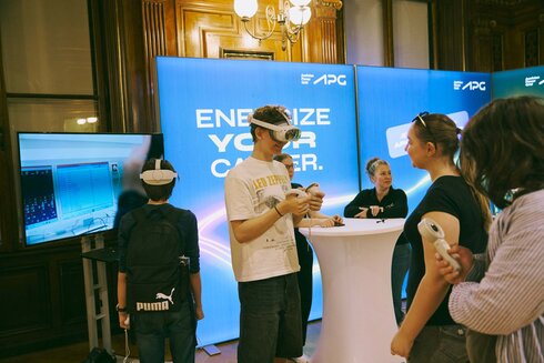 Menschen mit VR-Brillen interagieren an einem Stand mit Präsentationen.