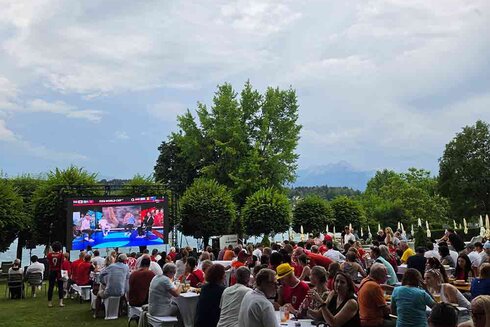 Die Menschen sitzen im Freien und schauen auf einen großen Bildschirm.