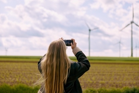 Eine Person mit langen Haaren fotografiert Windkraftanlagen auf einem Feld.