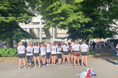 Gruppe von Frauen in Sportkleidung, die zum Publikum um einen Veranstaltungsort stehen.