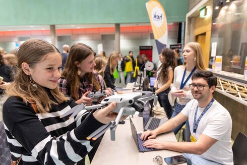 Mädchen hält eine Drohne, während andere an einem Messestand interagieren.