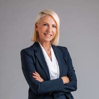 Professionelle Frau in Anzug, lächelnd, mit verschränkten Armen vor neutralem Hintergrund.