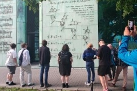 Gruppierung von Menschen betrachtet eine große Wand mit technischen Zeichnungen.