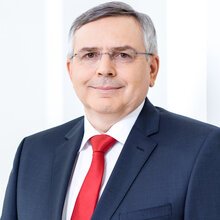 Porträt eines Mannes in Anzug mit Brille und roter Krawatte.