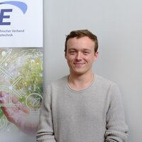 Ein Mann steht lächelnd vor einem Banner des Österreichischen Verbands für Elektrotechnik.