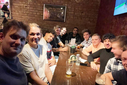 Gruppe junger Männer und Frauen posiert lächelnd an einem Tisch in einer Bar.