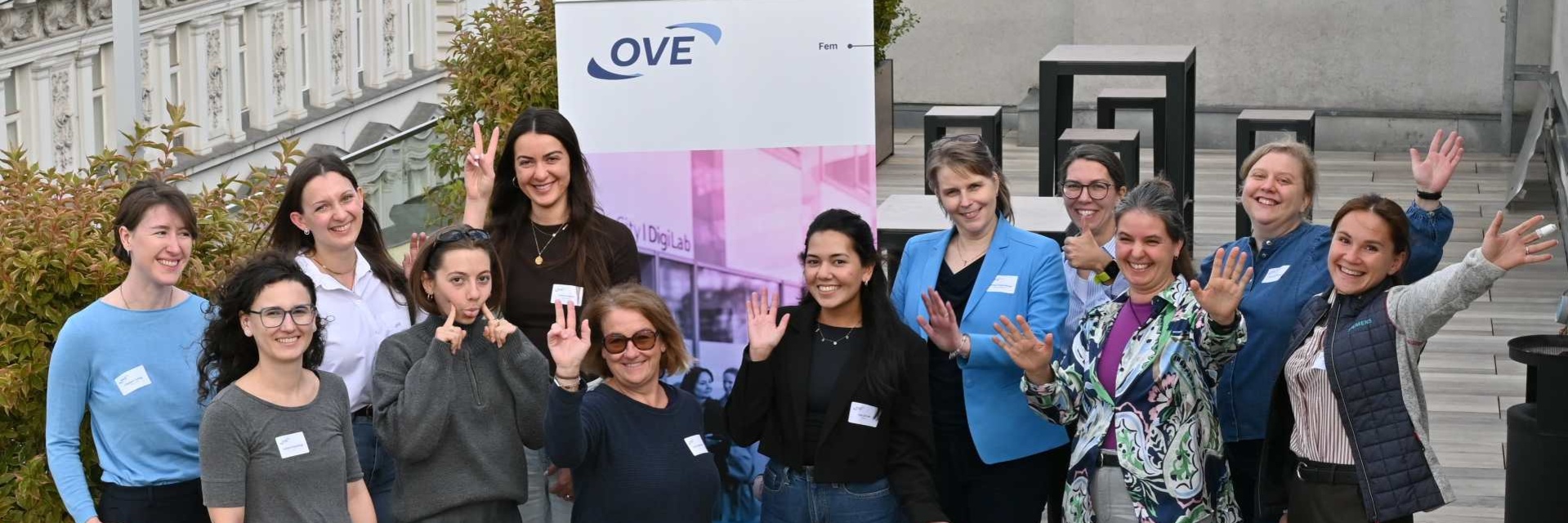 Gruppe von Frauen posiert fröhlich vor einem Banner auf einer Dachterrasse.