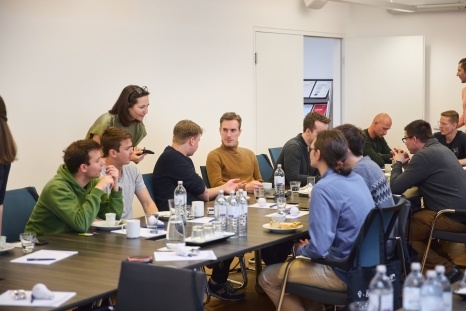 Gruppe von Menschen bei einer Besprechung an einem Tisch mit Getränken und Snacks.