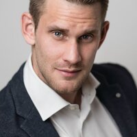 Porträt eines Mannes mit kurzem Haar in einem Anzug. Er schaut direkt in die Kamera.