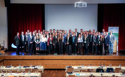 Gruppe von Personen auf einer Bühne bei einer Konferenz, mit Stühlen im Hintergrund.