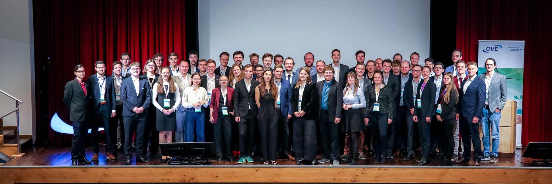 Gruppe von Personen auf einer Bühne bei einer Konferenz, mit Stühlen im Hintergrund.
