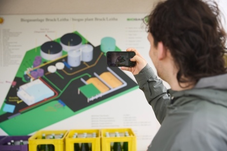 Person fotografiert eine Informationskarte eines geplanten Areals mit Containern.