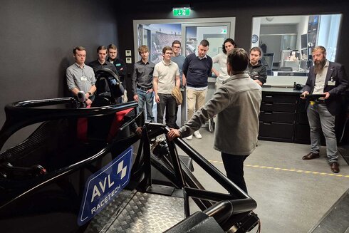 Gruppe von Menschen, die einem Vortrag über ein Rennauto lauschen.