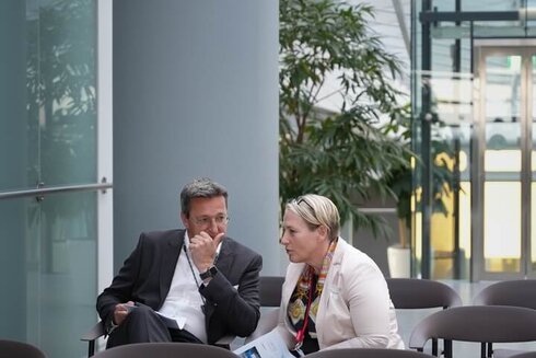 Zwei Personen sitzen in einem modernen Warteraum und sprechen miteinander.