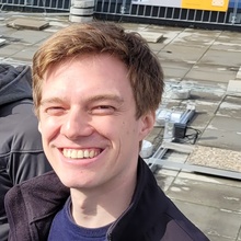 Junger Mann mit lächelndem Gesicht vor einem Baustellenhintergrund.