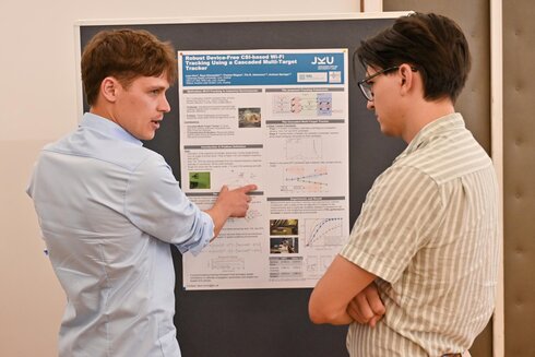 Zwei Personen diskutieren vor einem wissenschaftlichen Poster über Tracking-Technologie.