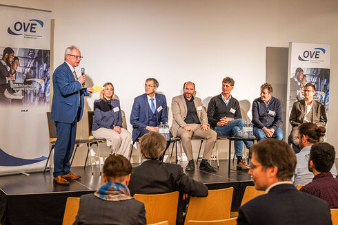 Podiumsdiskussion mit mehreren Sprechern und Publikum in einem Veranstaltungsraum.