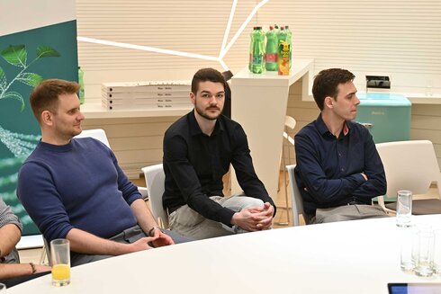 Drei Männer sitzen an einem Tisch und hören aufmerksam zu.