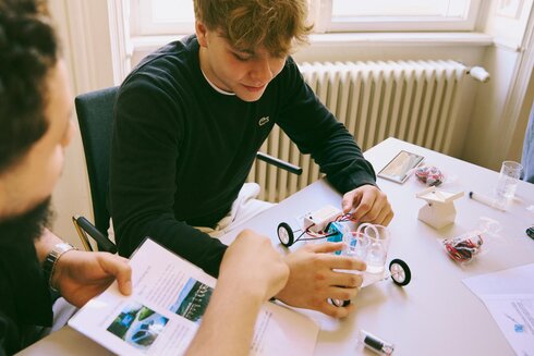 Zwei Personen bauen gemeinsam ein Modellauto aus verschiedenen Bauteilen.