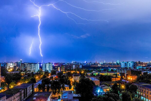 Blitz erhellt den Nachthimmel über einer Stadtlandschaft.