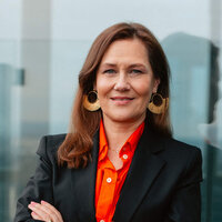 Eine Frau in formeller Kleidung lächelt mit den Armen verschränkt auf einer Terrasse.