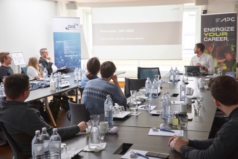 Besprechung in einem Konferenzraum mit Teilnehmern und Präsentation im Hintergrund.