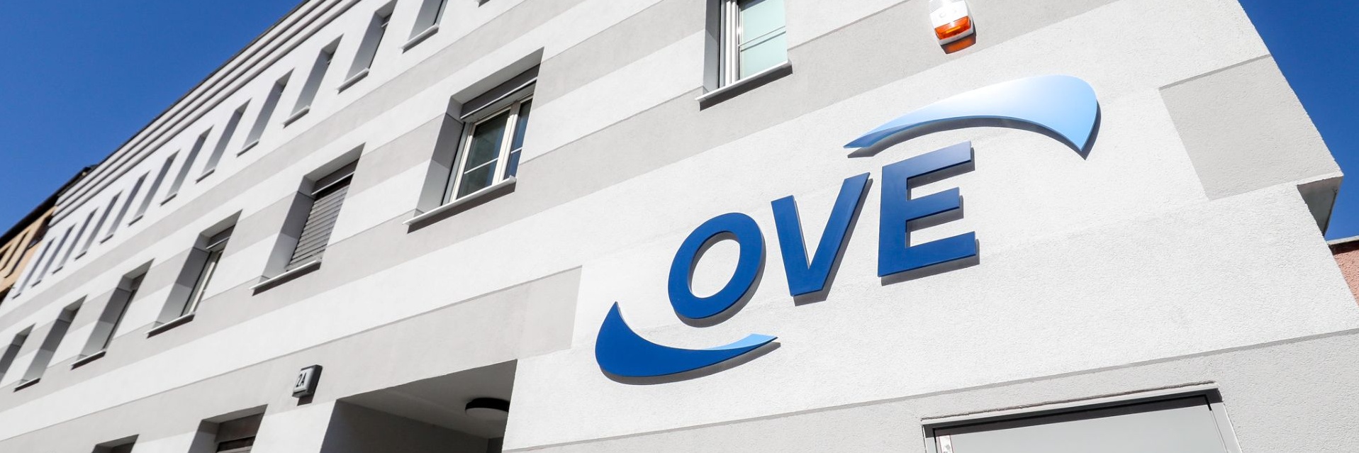 Gebäude mit grauer Fassade und dem Logo „OVE“ an der Wand.