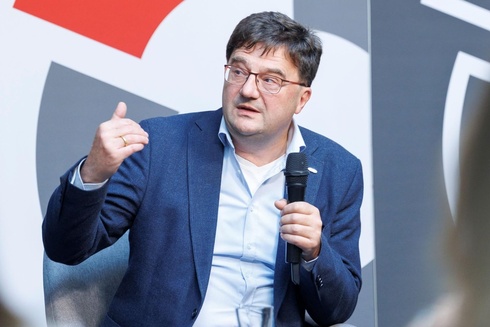 Ein Mann mit Brille und Mikrofon diskutiert auf einer Bühnenveranstaltung.