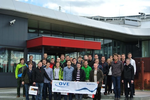 Gruppenfoto von etwa 40 Personen vor einem modernen Gebäude mit Banner.