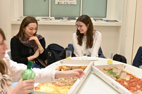 Zwei Frauen sitzen an einem Tisch mit mehreren Pizzakästen.