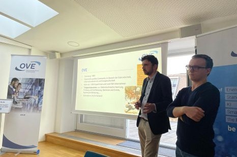 Zwei Referenten stehen vor einer Präsentationsfolie in einem Konferenzraum.